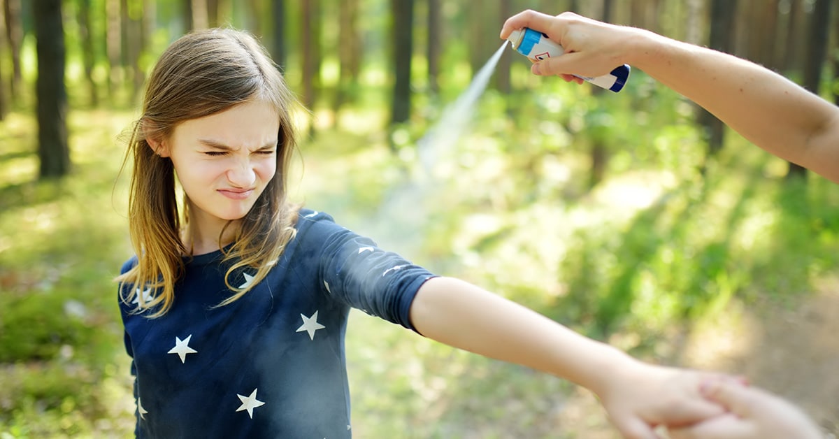 Woman spraying bug spray on child to prevent bug bites