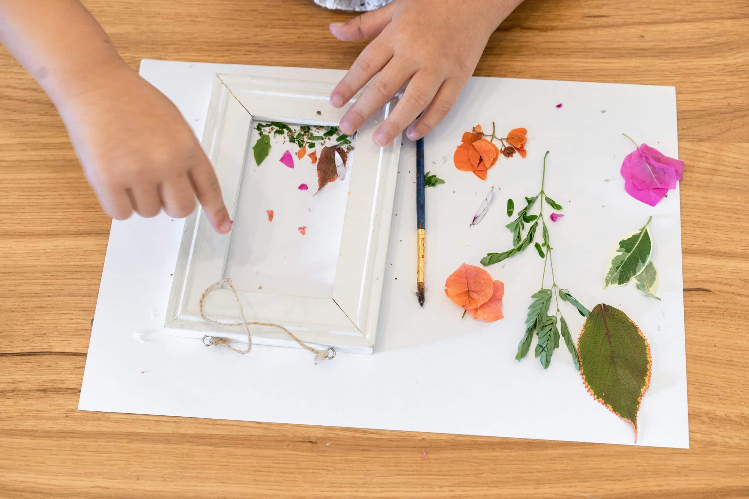 child placing flowers and leaves into a picture frame